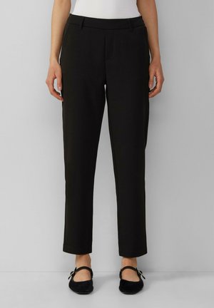 Pantalons noirs à coupe ajustée avec taille mi-haute, poches latérales et tissu lisse et léger. Modèle associé à des ballerines noires.