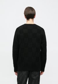 Juodas, tekstūruotas megztinis su languotu raštu. Apvalia apykakle, ilgomis rankovėmis ir laisvo kirpimo su ribbintais kraštais ir rankogaliais.