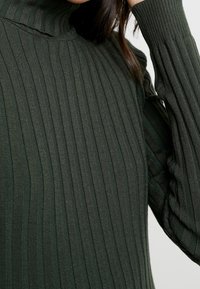 Grüner gerippter Rollkragenpullover mit enganliegendem Schnitt, strukturiertem Stoff und langen Ärmeln mit leichtem Stretch.