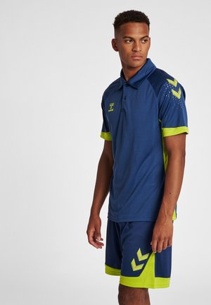 Navyblaues und grünes sportliches Poloshirt mit kurzen Ärmeln, das mit gemusterten Akzenten an den Schultern ausgestattet ist, kombiniert mit navyblauen Shorts und gelben Akzenten.