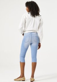 Pantalons capri en denim bleu clair au design ajusté, avec des fentes sur le côté à l'ourlet et des poches arrière, associés à une chemise blanche à boutons.