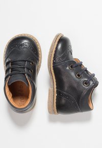 Scarpe in pelle nera con dettagli brogue, punta tonda e design con lacci. Suole in gomma beige chiaro e interni in pelle morbida.