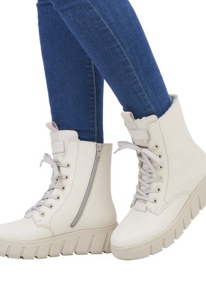 Weiße High-Top-Stiefel mit einer strukturierten matten Oberfläche, ausgestattet mit einem seitlichen Reißverschluss, runder Zehenform und dicker, geriffelter Gummisohle. Kombiniert mit blauen Jeans.