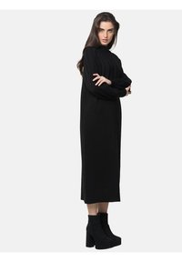 Robe en tricot côtelé noire avec un col montant et des manches longues. La robe a une silhouette droite, associée à des bottines à talons carrés noires.