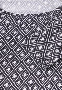 Chemise noir et blanc avec un motif en losange, caractérisée par des formes dessinées et une texture lisse. Encolure ronde avec des détails de couture visibles.