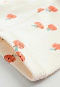 Weiches, cremefarbenes Material mit gerippter Textur, das verstreute orange Kürbisdesigns mit grünen Blättern zeigt. Am Rand gefaltet.