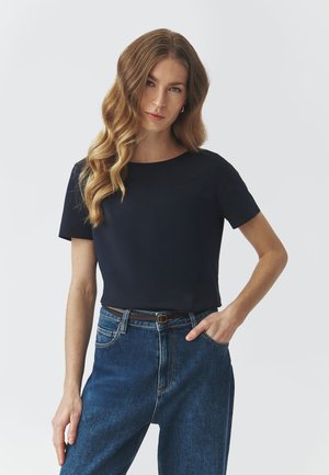 Navyblaues Kurzarmoberteil aus glattem Stoff mit rundem Ausschnitt, kombiniert mit hochtaillierten blauen Jeans und einem braunen Gürtel.