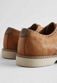 Ruske nahka-kengät sileällä pinnalla, joissa on reikähyväksytty muotoilu, beige pohja ja tumman kontrastivärin korko.