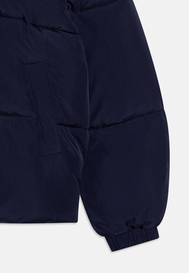 Ärmel einer marineblauen Steppjacke mit einem weichen, strukturierten Stoff, gerafften Bündchen und einer Seitenasche mit horizontaler Nahtverarbeitung.