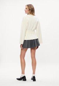 Biely opásaný kabát s dlhými rukávmi, v kombinácii s plisovanou šedou mini sukňou. Čierne topánky na vysokom podpätku a biele ponožky dotvárajú look.