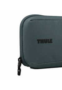 Custodia con cerniera Thule in tessuto grigio scuro, con superficie testurizzata, cuciture rinforzate e un logo nero ben visibile sulla parte anteriore.