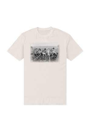Seks personer sidder på en stålbjælke højt over et bybillede, vist i sort og hvid på en lysebeige T-shirt.
