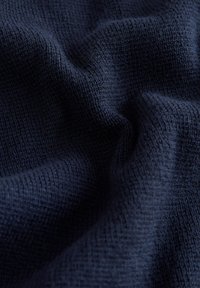 Tmavomodrá pletená látka s jemnou textúrou, zobrazujúca mäkké záhyby a jemné variácie v tkaní a hĺbke.