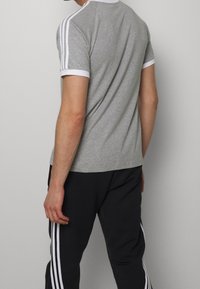 Grijze T-shirt van katoen, met witte gestreepte accenten op de schouders en mouwen. Gekleed met zwarte broek met witte zijstrepen.