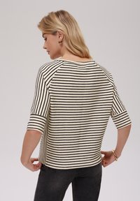 Striped top with black and cream horizontal stripes, 3/4 sleeves, round neckline, and a relaxed fit. Textured fabric with visible stitch details.