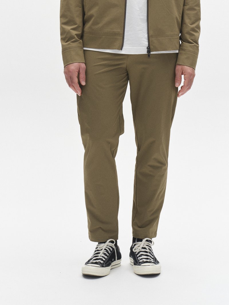 Pantalones ajustados color verde oliva hechos de tela ligera, con textura suave y bolsillos laterales, combinados con zapatillas altas negras.