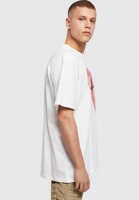 Hvid bomulds t-shirt med et stort pink grafisk design på forsiden. T-shirten har en afslappet pasform og korte ærmer.