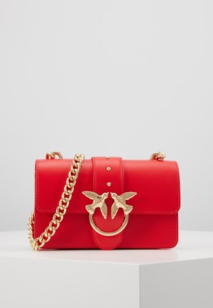 Sac d'épaule en cuir rouge avec une bandoulière en chaîne dorée, orné de deux ornements d'oiseaux dorés sur le fermoir avant et de trois petites clous dorés sur la bandoulière.