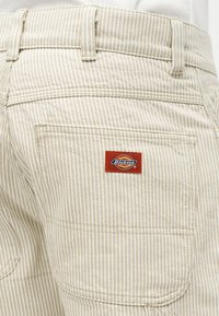 Pantalon beige et blanc à rayures avec une poche arrière dotée d'un écusson rouge du logo de la marque Dickies.