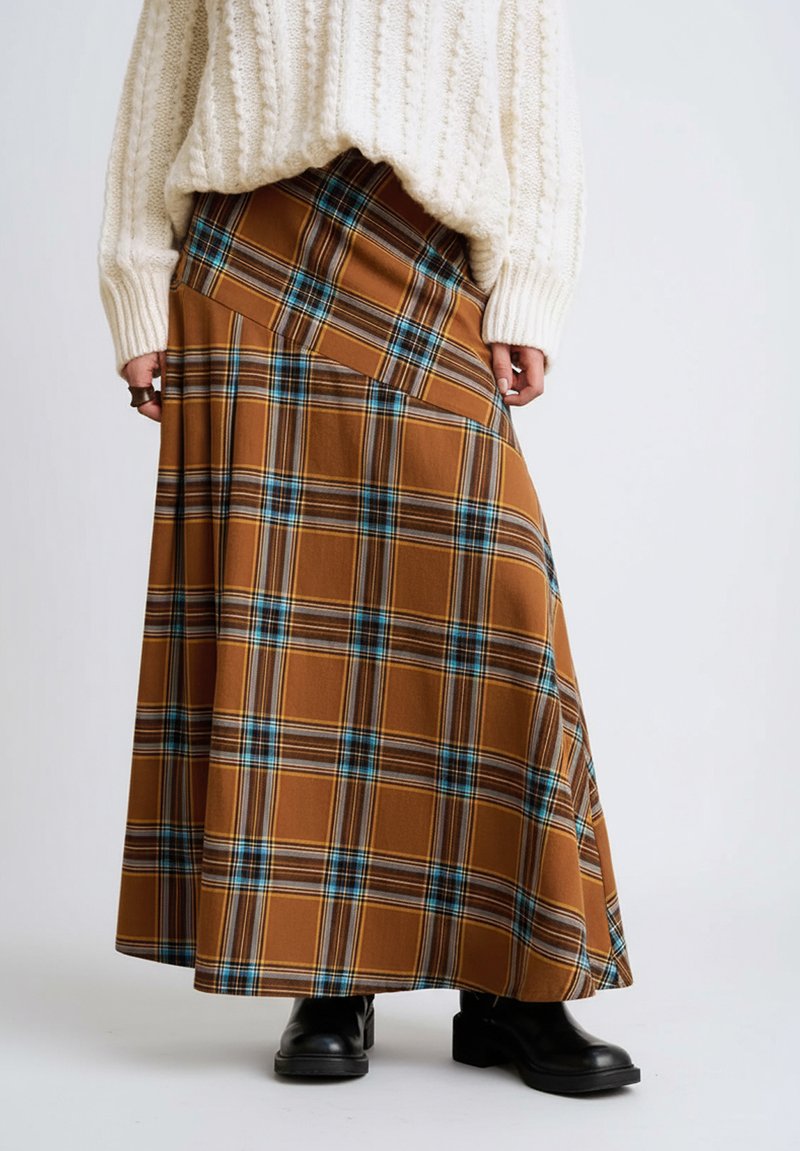 Długa spódnica w kratę w kolorze brązowym, z niebieskimi i żółtymi liniami, o pełnym kroju i bocznych plisach, zestawiona z czarnymi botkami za kostkę.