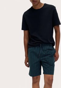 Marineblauw textuur T-shirt gecombineerd met groene gestreepte shorts met elastische tailleband en trekkoord. Casual en ademende outfit.