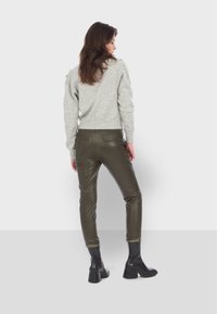 Šedý pletený svetr v kombinaci s tmavě zelenými koženými kalhotami, které mají ploché kapsy a zužující se nohavice, doplněný černými kotníkovými botami.