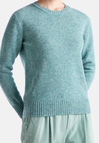Maglione lavorato a maglia di un azzurro chiaro, con scollatura a girocollo, polsini e orlo a coste. Texture morbida con un leggero aspetto melangiato.