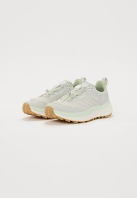 Baskets de trail running gris clair avec un mesh texturé, des accents verts doux, des semelles en caoutchouc robustes et des lacets réfléchissants pour plus de visibilité.