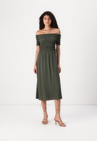 Off-shoulder, olivgrön klänning med rynkad kropp och flödig midi-kjol. Bärs med gyllene sandaletter med remmar. Slät textur.