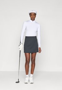 Camisola branca de mangas compridas com detalhes pretos, combinada com uma saia cinzenta. Os acessórios incluem uma boné branco e um taco de golfe. Usado com ténis brancos.