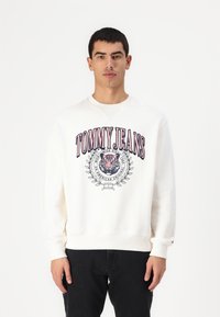Witte sweatshirt met een groot "TOMMY JEANS" logo in rood en blauw, een gecentreerd beeld van een tijger, en geribbelde manchetten en zoom.