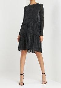 Black, long-sleeve dress with a tiered design and subtle shimmer. Features a round neckline and a flowing A-line silhouette.