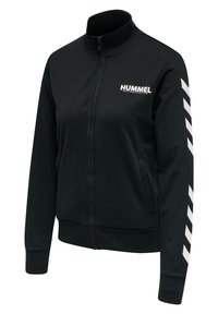 Czarna kurtka sportowa na zamek z wysokim kołnierzem, białe logo "HUMMEL" na piersi oraz białe paski w kształcie chevron na rękawach. Gładka textura, dopasowany krój.