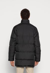 Svart puffjacka med hög krage, med ett quiltat mönster och långa ärmar. Mjuk, slät textur med avslappnad passform.