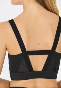 Mustat urheilurintsikat, joissa on leveät elastiset hihnat, verkko-osio selässä ja tiukka muotoilu tuen tarjoamiseksi. Suora kangas.