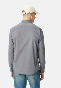Camicia a maniche lunghe grigia con motivo, realizzata in un tessuto leggero, con polsini con bottoni e orlo dritto, indossata con jeans blu sbiaditi.