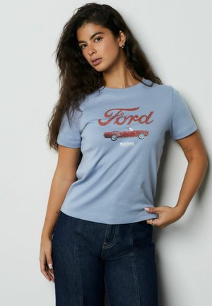 Világoskék pamut póló, amelyen egy piros "Ford" logó és egy piros kabrió autó grafikája látható, rövid ujjakkal és kerek nyakkivágással.