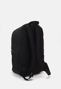 Mochila preta com exterior de tecido liso, painel traseiro acolchoado, correias ajustáveis e um bolso lateral em malha para armazenamento.