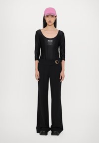 Bodysuit negro ajustado con mangas de tres cuartos y estampado de logo, combinado con pantalones anchos de tiro alto en negro y una gorra rosa.