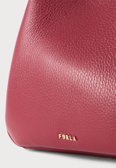 Детайлен кадър на червена кожена чанта Furla с текстура и малки златисти букви на логото близо до основата.