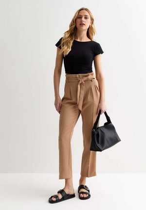 Maglietta nera aderente, pantaloni beige a vita alta con cintura annodata, borsa nera e ciabatte nere. Tessuto liscio, taglio dritto.