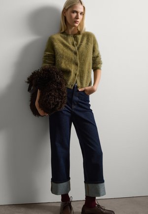Cárdigan esponjoso verde oliva con cuello redondo y botones, combinado con vaqueros anchos de denim oscuro con dobladillo y zapatos marrones.