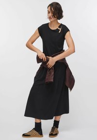 Robe noire à manches courtes avec jupe froncée. Associée à une veste en cuir marron nouée autour de la taille et à des baskets noires à imprimé léopard.