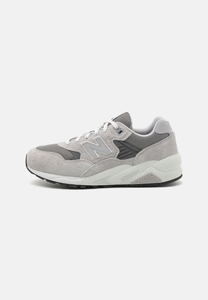 Zapatillas gris claro con parte superior de ante y malla, que cuentan con un collarín acolchado, cordones blancos y una suela de goma negra contrastante.