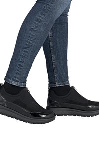 Baskets noires de sport avec une surface texturée, dotées d'une fermeture éclair et d'accents brillants, associées à un jean en denim foncé.