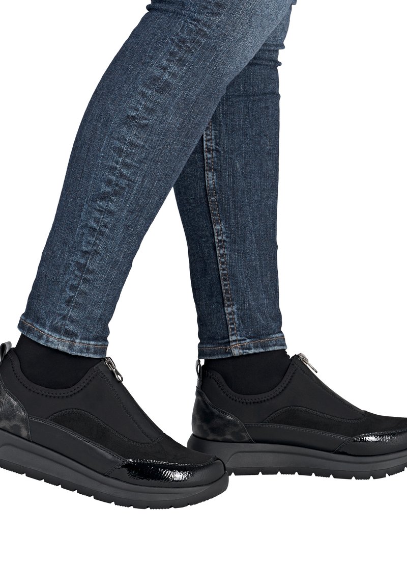 Baskets noires de sport avec une surface texturée, dotées d'une fermeture éclair et d'accents brillants, associées à un jean en denim foncé.