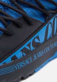 Μπλε υφασμάτινο πάνω μέρος με μαύρες λεπτομέρειες και κορδόνια. Φέρει έντ ονο λογότυπο "VERSACE JEANS COUTURE", ελαστική σόλα με υφή.