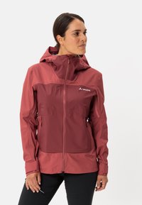 Giacca impermeabile rossa con una vestibilità aderente, cappuccio regolabile, tasche con zip e tessuto testurizzato. Logo esposto sul petto.