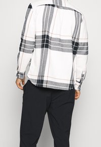 Camicia a maniche lunghe a quadri in bianco, grigio e nero con dettagli rosa chiaro; tessuto morbido, orlo arrotondato, polsini con bottone e dettaglio sulla parte posteriore.