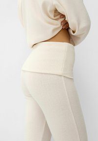 Cream-colored loungewear set featuring a ribbed waistband and soft, textured fabric, with fitted pants and a relaxed, cropped top design.